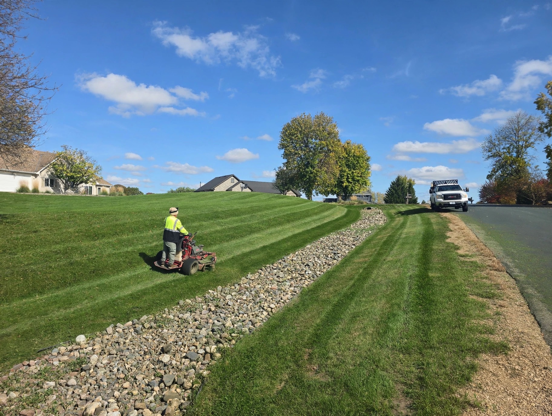 Green Planet crew member mowing a sunny hillside lawn with a walk-behind mower